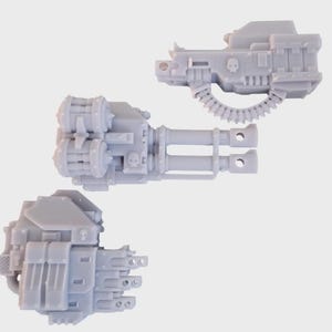 May include: Three light gray miniature weapon models. The models include a double-barreled gun, a single-barreled gun with a belt of ammunition, and a weapon with a boxy design. Each model has intricate details and a skull emblem.