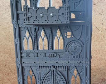 May include: A gray, multi-level miniature building with arched windows, a balcony, and decorative details. The structure features a large arched doorway and circular design elements, suitable for tabletop gaming.