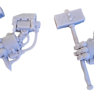 Könnte beinhalten: Zwei graue Plastik-Miniaturroboterarme, die eine Hammerwaffe halten. Der Hammer hat einen rechteckigen Kopf mit einem erhabenen Pfeilmotiv.