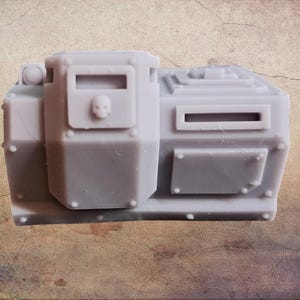 May include: A grey miniature armoured vehicle component with a skull emblem. The model features rectangular and square shapes, with rivet details and a small, rectangular window. The overall design suggests a military or sci-fi theme.