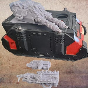 May include: A black and red model tank with two large grey gun barrels and additional grey components. Two detached grey gun components are in front of the tank. The tank has red and blue accents.