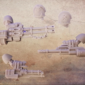Könnte beinhalten: Mehrere unbemalte, hellgraue Miniaturwaffen und Helme aus Kunststoff. Das Bild zeigt drei Miniaturmaschinengewehre mit verschiedenen Designs und zwei Helme. Die Waffen weisen detaillierte Merkmale auf, darunter Läufe, Ketten und Visiere. Die Helme haben eine abgerundete Form.