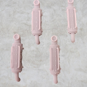 Può includere: Quattro massaggiagengive rosa in silicone per bambini, ciascuno con un corpo cilindrico, un lato strutturato e una parte superiore e inferiore arrotondata. I massaggiagengive sono disposti su uno sfondo grigio screziato.