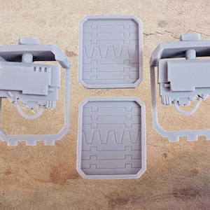 May include: Four light grey plastic miniature weapon models and two rectangular shield models. The weapons have a complex design with a barrel, a boxy body, and a frame. The shields have a textured surface.