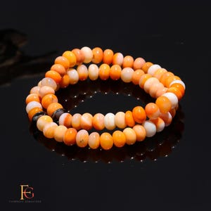 May include: A double-strand bracelet made of orange and white shell beads. The bracelet has a dark grey accent bead.