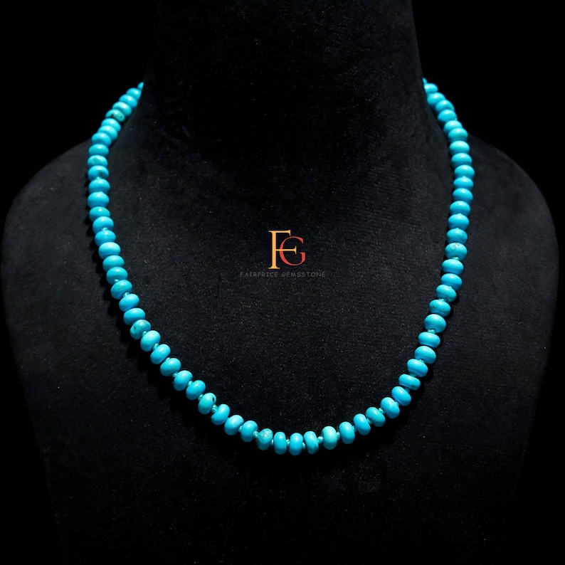 May include: A turquoise bead necklace displayed on a black mannequin. The necklace is composed of small, round, light blue beads. The beads are strung together to form a complete necklace. The background is black.