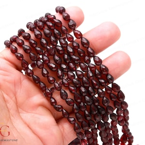 May include: A strand of deep red gemstone beads, each bead is faceted and shaped like a teardrop. The beads are strung on a clear thread and are approximately 8mm in size.