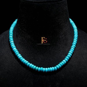 Op de afbeelding: Een turquoise kralenketting tentoongesteld op een zwarte mannequin. De ketting bestaat uit kleine, ronde, lichtblauwe kralen. Het Fairprice Gemstone-logo is rechtsonder zichtbaar.