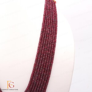 May include: A strand of red gemstone beads, likely ruby, arranged in a long, straight line. The beads are small and uniform in size, creating a smooth and elegant look.
