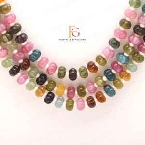 May include: Multicoloured gemstone beads in a variety of shapes and sizes, including round, oval, and teardrop. The beads are strung on a white cord and are arranged in a layered pattern. The beads are a mix of pink, green, brown, and yellow.