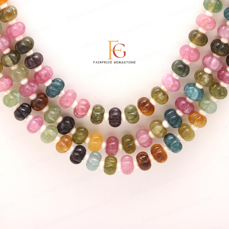 May include: Multicoloured gemstone beads in a variety of shapes and sizes, including round, oval, and teardrop. The beads are strung on a white cord and are arranged in a layered pattern. The beads are a mix of pink, green, brown, and yellow.