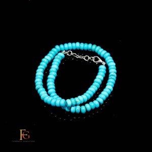 Op de afbeelding: Een turquoise kralenketting met een zilveren sluiting. De ketting bestaat uit kleine, ronde, lichtblauwe kralen. De sieraden worden tegen een zwarte achtergrond getoond.