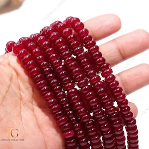 May include: A strand of deep red gemstone beads, likely carnelian, with a smooth, polished finish. The beads are round and uniform in size, creating a consistent look. The strand is displayed on a hand, showcasing the beads' colour and texture.