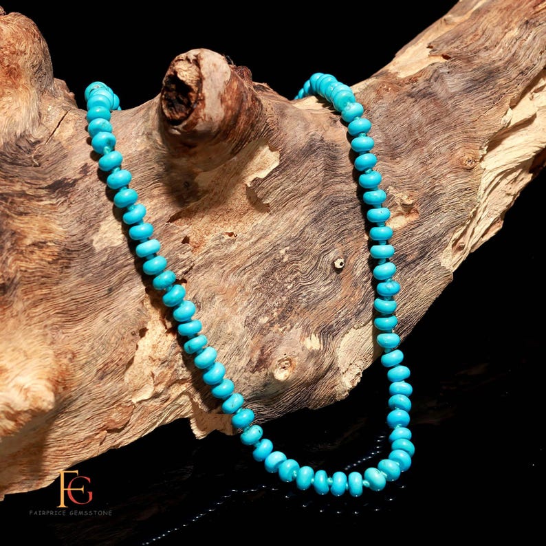 May include: A turquoise gemstone necklace composed of small, round beads. The necklace is displayed on a piece of weathered wood, with a dark background. The beads are a vibrant, consistent blue-green color.