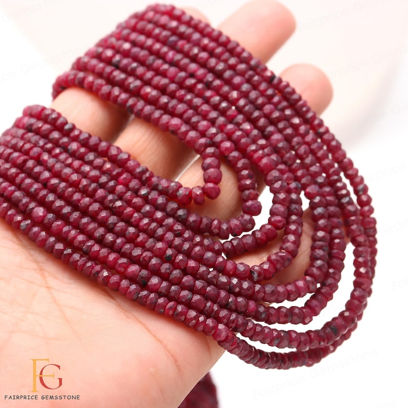 May include: A strand of deep red ruby beads, faceted and round, strung together on a white background. The beads are approximately 3mm in diameter and have a smooth, polished finish.