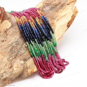 Puede incluir: Una hebra de cuentas de piedras preciosas en colores rojo, verde, azul y amarillo. Las cuentas están dispuestas en un patrón de arcoíris y están enhebradas en un alambre delgado. Las cuentas se muestran en una pieza de madera.