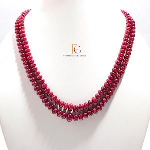 Op de afbeelding: Een dubbele ketting bestaande uit kleine, ronde, dieprode edelstenen. De ketting wordt getoond op een witte mannequin. De tekst "FAIRPRICE GEMSTONE" is zichtbaar in de afbeelding.