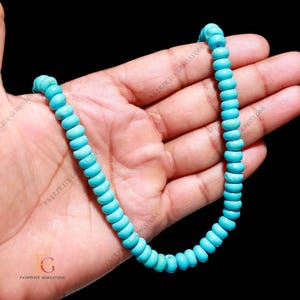 Op de afbeelding: Een ketting van turkoois edelsteen kralen. De kralen zijn helder lichtblauw van kleur en cilindrisch van vorm. De kralen zijn aan elkaar geregen. De achtergrond is zwart.