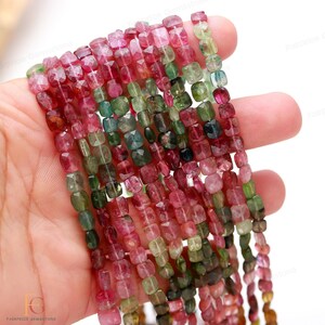 May include: A strand of multi-colored square-shaped gemstone beads. The beads are a mix of pink, green, and black.