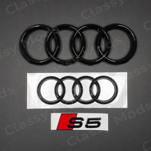 May include: Black Audi emblem with four interlocking rings, a black Audi emblem with four interlocking rings on a white background, and a red and black S5 emblem.