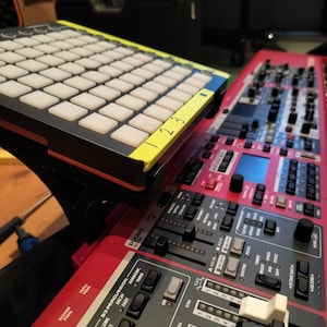 May include: A red electronic keyboard with a black and white pad controller on top. The keyboard has a variety of buttons and knobs, including a volume knob, a sustain pedal, and a piano section. The pad controller has a yellow and blue design with the numbers 1, 2, and 3 printed on it.