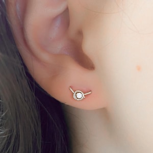 Pode incluir: Um close-up de um brinco de argola de prata com um pequeno diamante no centro. A argola é curva e tem um design simples.