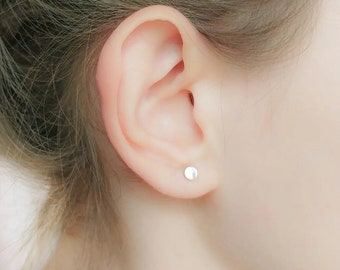 May include: A close-up of a person's ear with a small, round, silver earring.