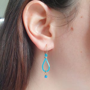 May include: A pair of turquoise blue dangle earrings with a gold hoop and a small turquoise blue bead at the bottom.
