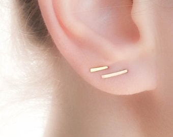 May include: A pair of gold bar earrings, worn in the upper lobe of an ear.