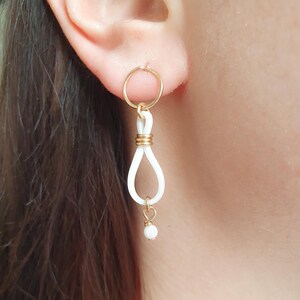 May include: White ceramic earrings with a gold hoop and a small white bead dangling from the bottom.