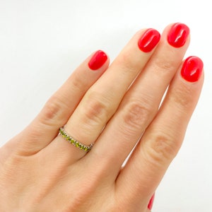 May include: A silver ring with a row of small green gemstones. The ring is on a finger with red nail polish.