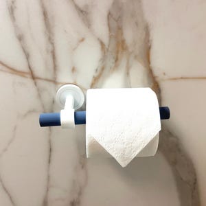 May include: A white toilet paper roll on a blue and white holder. The holder is mounted on a marble wall. The toilet paper is white and has a textured pattern.