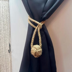 May include: A black curtain with a natural rope tieback featuring a knotted ball at the end.