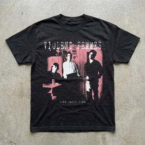 May include: Black t-shirt featuring a band photo in pink and black. The band's name, "VIOLENT FEMMES," is printed above the image, with "GONE DADDY GONE" below. The shirt has a crew neck and short sleeves.