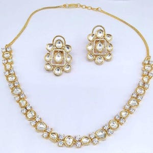 Könnte beinhalten: Eine goldene Halskette mit einer zarten Kette und einer Reihe von klaren, facettierten Steinen. Die Halskette wird mit passenden Ohrringen im gleichen Design geliefert.