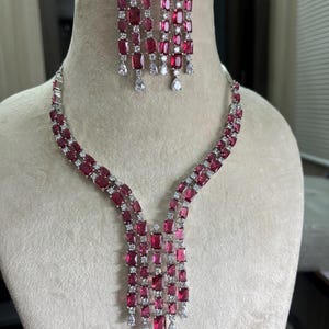Peut inclure: Un collier et des boucles d'oreilles en argent avec un design en cascade de pierres de zircone cubique rouges et claires.