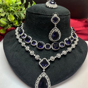 Peut inclure: Un ensemble de collier et boucles d'oreilles en argent avec un grand pendentif en forme de larme. Le collier comporte deux rang&eacute;es de petites pierres carr&eacute;es et le pendentif et les boucles d'oreilles pr&eacute;sentent de grandes pierres bleu fonc&eacute;.