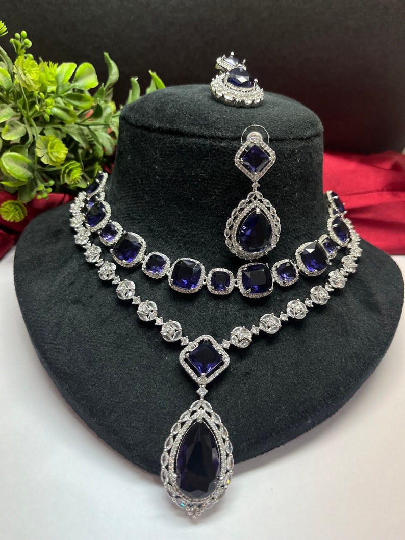 Peut inclure: Un ensemble de collier et boucles d'oreilles en argent avec un grand pendentif en forme de larme. Le collier comporte deux rang&eacute;es de petites pierres carr&eacute;es et le pendentif et les boucles d'oreilles pr&eacute;sentent de grandes pierres bleu fonc&eacute;.