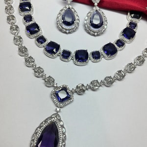 Peut inclure: Un ensemble de collier et boucles d'oreilles en argent avec un grand pendentif en forme de larme. Le pendentif et les boucles d'oreilles pr&eacute;sentent une grande pierre pr&eacute;cieuse violette fonc&eacute;e entour&eacute;e de petites pierres pr&eacute;cieuses claires.