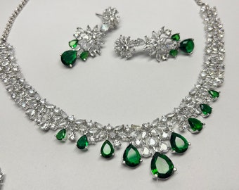 May include: A silver necklace and earrings set with a floral design and green pear-shaped stones.