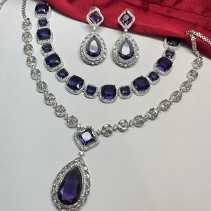 Peut inclure: Un ensemble de collier en argent avec un pendentif en forme de larme et deux colliers plus petits avec des pierres de forme carr&eacute;e. Les pierres sont d'une couleur violet fonc&eacute;.
