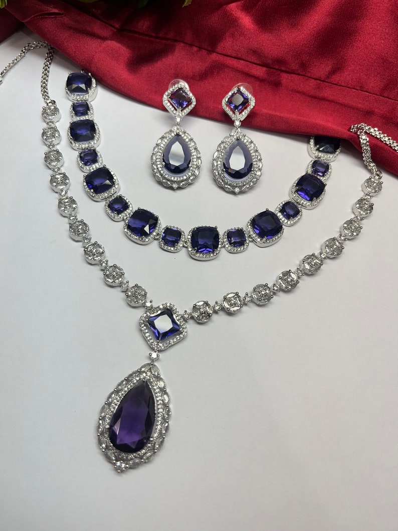Peut inclure: Un ensemble de collier en argent avec un pendentif en forme de larme et deux colliers plus petits avec des pierres de forme carr&eacute;e. Les pierres sont d'une couleur violet fonc&eacute;.