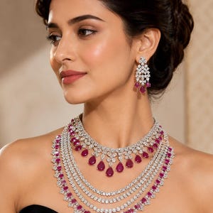 Puede incluir: Un collar de varias capas en metal plateado con piedras blancas transparentes y gemas de color rosa intenso en forma de lágrima. Incluye pendientes colgantes a juego con un diseño floral y una piedra rosa en forma de lágrima.