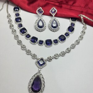 Peut inclure: Un ensemble de collier en argent avec un grand pendentif en forme de larme et deux plus petits pendentifs carr&eacute;s, tous sertis de pierres pr&eacute;cieuses violettes. L'ensemble comprend &eacute;galement une paire de boucles d'oreilles assorties avec des pierres pr&eacute;cieuses violettes en forme de larme.