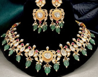 May include: A gold necklace and earrings set with a traditional Indian design. The necklace features a large, round, clear stone surrounded by smaller stones and green and white beads. The earrings have a similar design with a smaller, round, clear stone.