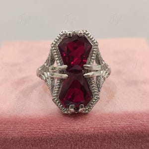 May include: A silver ring featuring a large, faceted, dark red gemstone set in a geometric design.
