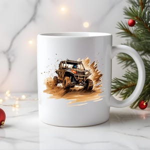 May include: White ceramic mug with a graphic of a brown and black off-road vehicle driving through mud. The vehicle has a black roll cage and a black driver's seat.