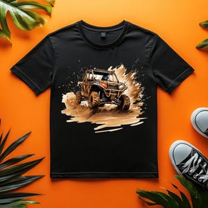 May include: Black t-shirt with a graphic print of a brown off-road vehicle driving through mud. The vehicle has a black roll cage and a black and orange color scheme.