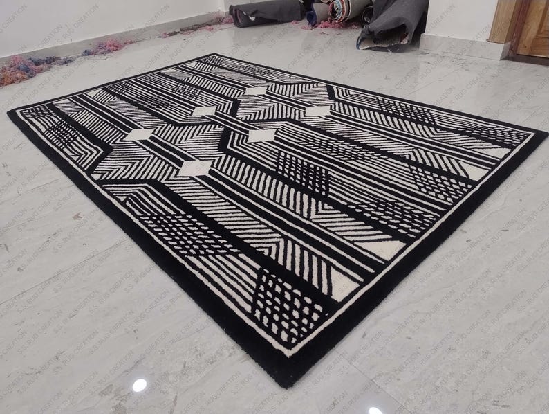 Może przedstawiać: Czarno-biały dywan w geometryczne wzory o nowoczesnym designie. Dywan ma białe tło z czarnymi liniami i kształtami.