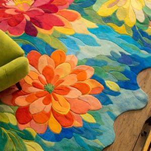 May include: A colorful floral rug featuring large, stylized flowers in shades of orange, red, yellow, and blue. The rug has a unique, organic shape and is placed on a wooden floor. A green armchair is partially visible in the upper left corner.